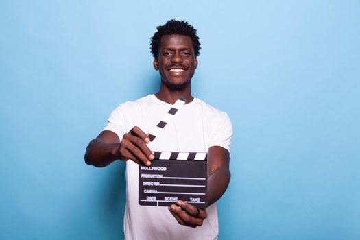 Portrait of man holding clapperboard to cut scenes in movie making industry. Young adult showing chalkboard to camera and smiling while having filmmaker object for cinematography