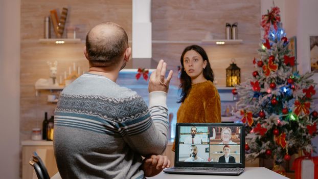 Businessman using video call for work on christmas eve and woman being impatient about celebrating holiday festivity. Husband working from home on laptop while wife preparing for celebration