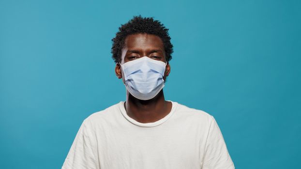 Portrait of african american man wearing face mask to protect from coronavirus in studio. Close up of black person looking at camera while having protective mask on face over background.