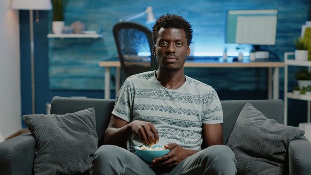 POV of person watching football game on television at home. Adult enjoying sports play and cheering to win while looking at camera and eating popcorn. Man relaxing with TV screen