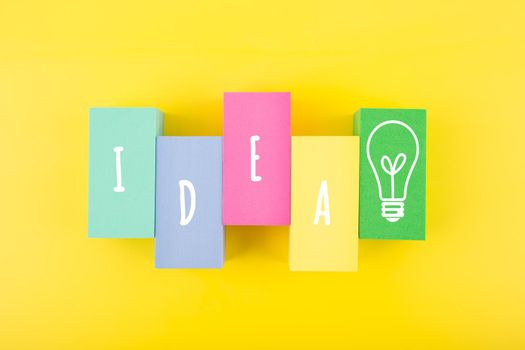 Concept of idea, creativity, start up or brainstorming. Single word idea and light bulb written on multicolored rectangles in a row on bright yellow background