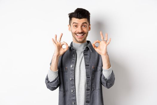 Happy guy say yes, smiling and showing okay signs, like good product, nod in approval and make satisfied face, praise excellent work, standing on white background.