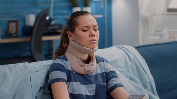 Close up of woman wearing cervical neck foam feeling sick and holding capsule tablet for treatment. Ill adult with medical collar to heal muscle and vertebra injury. Injured person in pain