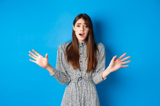 Sad and gloomy woman in dress facing failure, looking distressed and sighing upset, losing and standing on blue background.