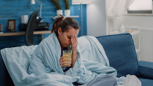 Sick woman with headache drinking effervescent vitamin drink to cure cold and flu. Adult with glass of medication as disease treatment having virus symptoms. Person with illness