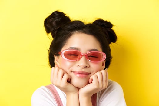 Summer fashion concept. Dreamy asian girl with romantic face expression, daydreaming or imaging something beautiful with closed eyes and happy smile, wearing sunglasses.