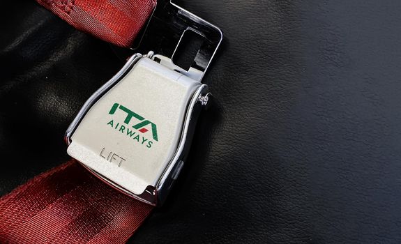 Rome, IT, October 2021: Red lap belt of an empty seat inside an airplane with the ITA Airways logo printed on the metal. ITA Airways is the new Italian flag carrier starting from 15 October 2021