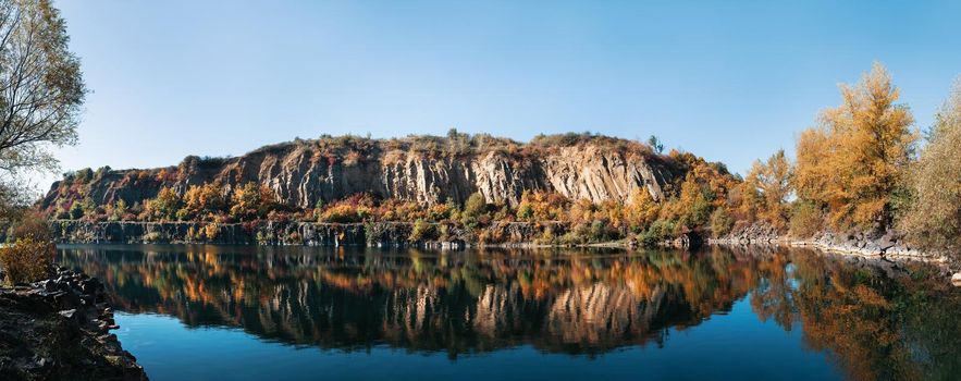 Golden autumn with colourful trees in old flooded quarry. Rocks, lake and yellow trees