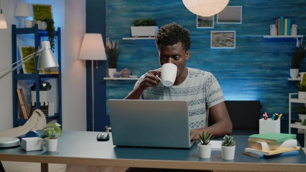 Freelance employee working from home on laptop and typing. Man doing remote corporate business work with technology while drinking cup of coffee. Networking entrepreneur with notebook