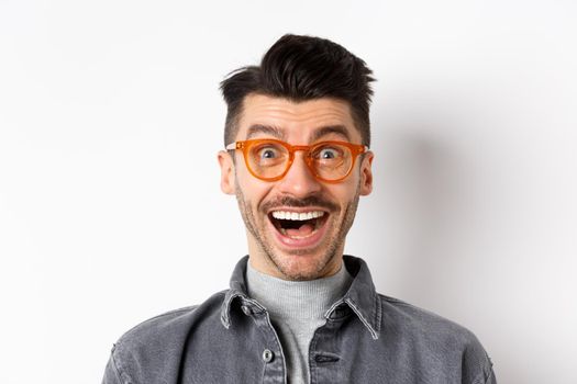 Excited funny man in glasses smiling, look with amazement and joy at awesome promo, standing happy against white background.