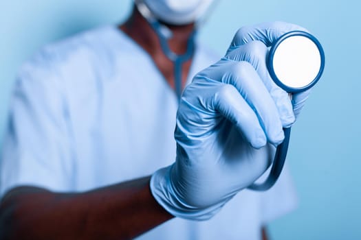 Close up of african american hand holding stethoscope while wearing gloves for healthcare protection. Black nurse with uniform having medical instrument in hand for heartbeat examination