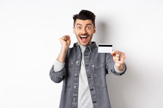 Happy man scream from excitement and show plastic credit card, recommending bank, standing on white background.