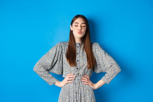 Valentines day and relationship concept. Romantic woman with closed eyes kissing lover, pucker lips and kissing you, standing on blue background.