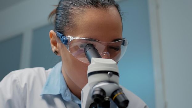 Close up of scientist checking microscopic tool with sample tray in laboratory. Woman using microscope with magnifying lens used for optical dna investigation in medical research industry