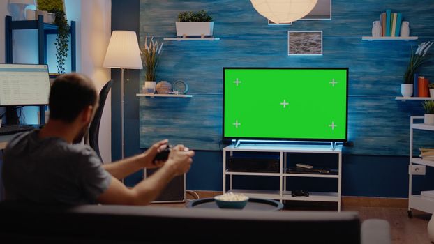 Man using joystick on green screen background display on television at home. Mockup digital template with isolated media used as chroma key. Person playing with controller in modern flat