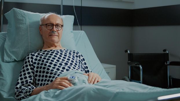 Portrait of old patient with disease sitting at hospital ward in bed with nasal oxygen tube for medical health problems. Man waiting on doctor and nurse for treatment and consultation