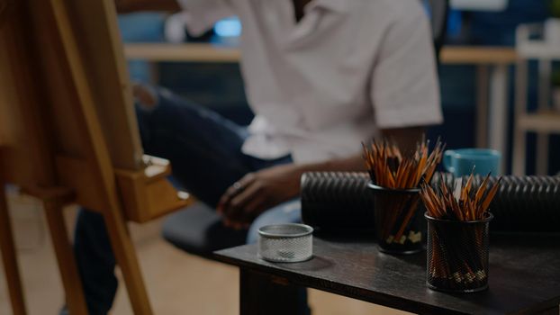 Close up of colorful pencils for art concept and drawing on canvas in workshop space. African american person in background using professional tools for modern masterpiece project