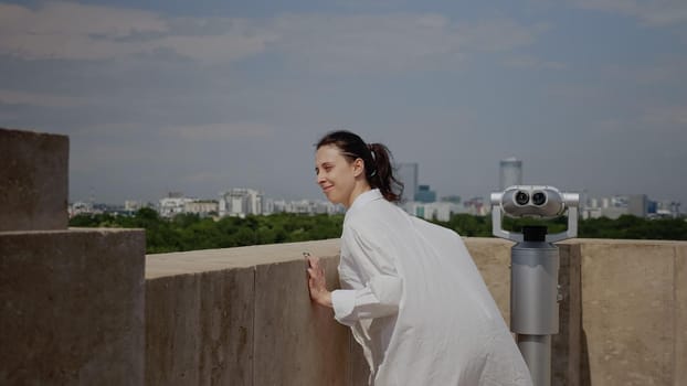 Caucasian woman admiring panoramic view of modern town while standing on top of skyline tower. Young adult looking at urban landscape from observation point on high building roof