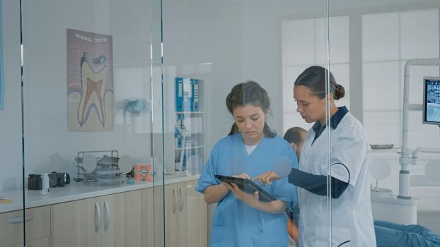 Professional team of stomatologists looking at digital tablet for dentition analysis and diagnosis in dental office. Dentist and nurse using modern technology and dentistry equipment