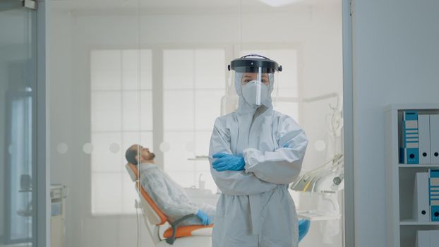 Portrait of dentist standing in hazmat suit for virus protection at oral clinic. Caucasian woman wearing coverall ppe prepared for dentistry operation and surgical consultation