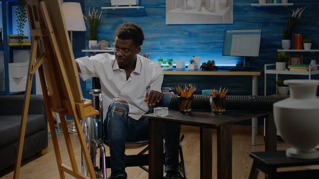 Disabled african american man using pencil for drawing design sitting in artwork space. Black person in wheelchair with artistic imagination creating modern masterpiece for fine art project