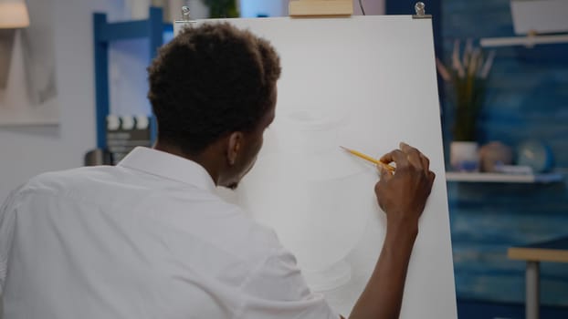 Young black artist using art pencil on canvas for vase drawing hobby in workshop room at home. African american person with artistic imagination creating masterpiece for fine art