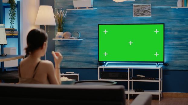 Green screen on modern television display at home in living room. Caucasian young woman watching chroma key for copy space template and isolated mockup background on media device