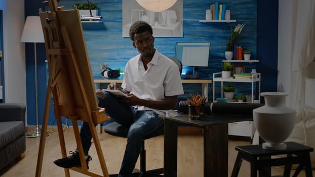 Man of african american ethnicity designing sketch for vase drawing on white canvas and easel in workshop studio. Black artist with creativity and imagination creating art masterpiece