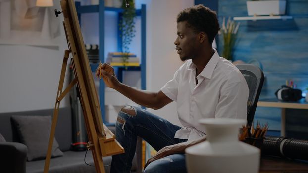 Adult of african american ethnicity drawing vase on canvas using pencil while sitting in art studio at home. Black young person with artistic imagination creating modern masterpiece