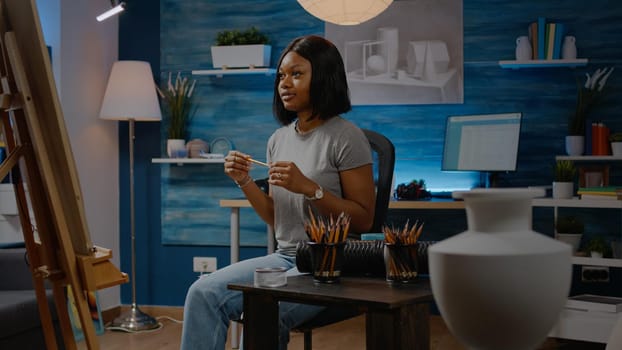 Black young artist working on vase drawing at home in artwork studio. African american woman using art tools, pencil and white canvas on easel creating authentic masterpiece as hobby