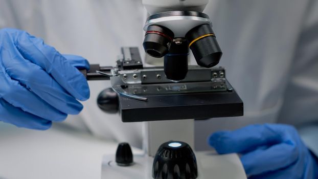 Close up of specialist hands using microscope tool in microbiology laboratory. Researching instrument with magnifying glass, optical lens and tray for dna sample in chemical industry