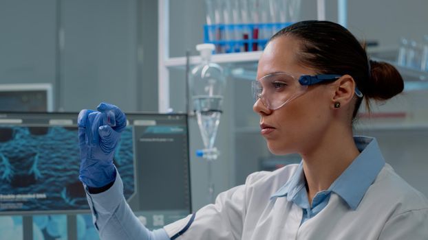 Chemistry specialist analyzing blood sample on glass in laboratory. Technician woman with glasses and gloves wearing lab coat while holding instrument with plasma for medical diagnostic