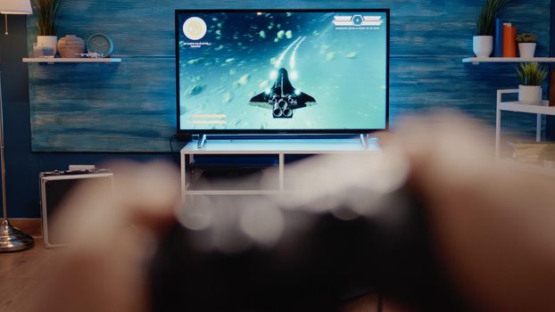 Close up of television display with action video games on console while person holding joystick playing for leisure and hobby. POV of simulator player sitting at home with modern technology