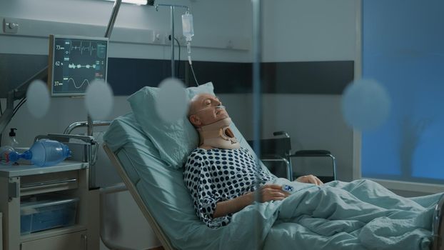 Sick patient recovering from injury with cervical collar for neck in hospital ward at medical unit. Old man in modern intensive care room sitting in bed with oximeter and oxygen tube