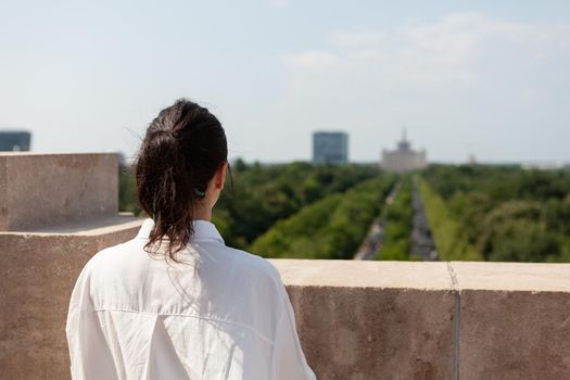 Woman toursit standing on building rooftop enjoying seeing panoramic view of metropolitan city during summer vacantion. Landscape with urban buildings from observation point