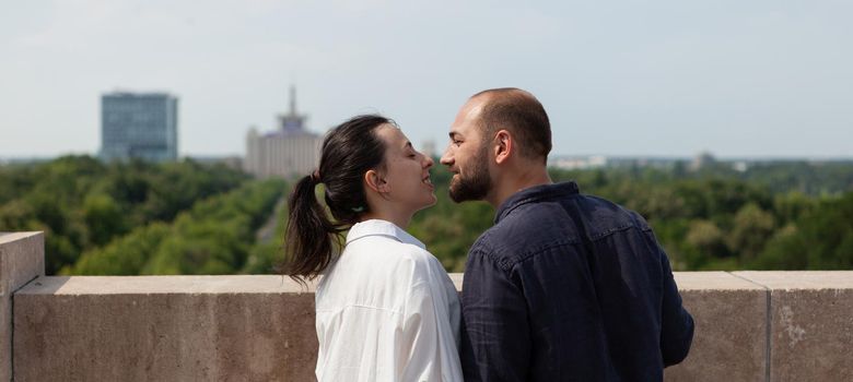 Lovers happy couple kissing on tower rooftop celebrating relationship anniversary standing at observation point enjoying beautiful metropolitan city view. Landscape with urban buildings