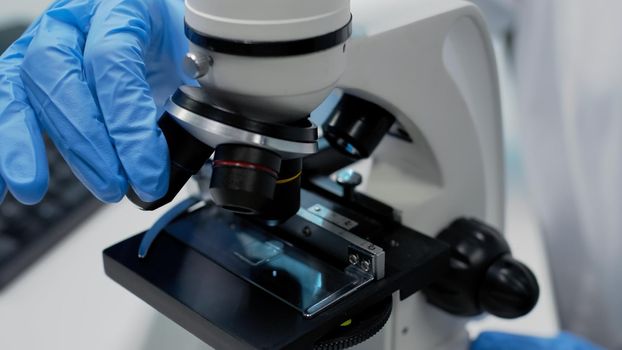 Close up of microscopic glass tray on optical instrument in laboratory. Biology tool used for dna examination and checking bacteria. Doctor hands fixing sample plate for investigation