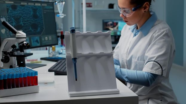 Close up of scientist using micropipette at laboratory desk for chemical research in medical industry. Biochemistry doctor with computer, vacutainer and scientific equipment wearing lab coat