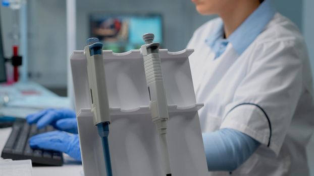 Close up of biochemist using micropipette in laboratory for scientific analysis in healthcare industry. Professional doctor in lab coat with liquid dropper on desk used for development