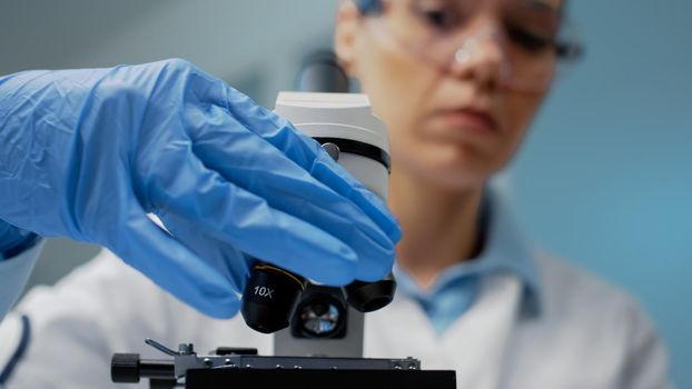 Close up of doctor using optical lens on microscope in biochemistry laboratory. Specialist using microscopic magnifying glass instrument for dna investigation and genetic bacteria