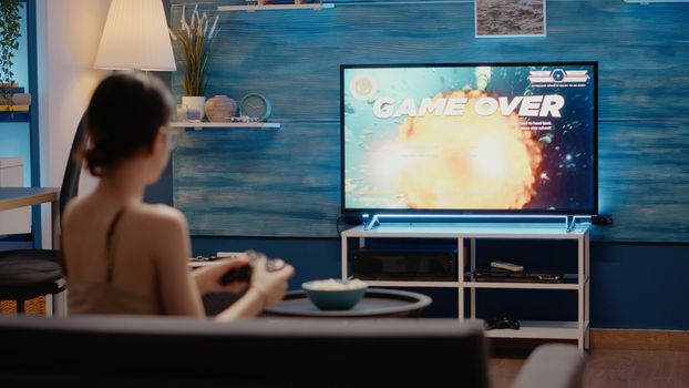 Caucasian woman losing while playing video games holding controller sitting in living room for digital cyberspace reality indoors. Person using virtual technology for entertainment