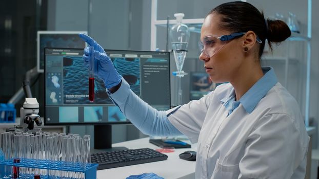 Doctor working in science laboratory with test tubes and chemical equipment. Chemist with lab coat and gloves holding flask filled with blood or red solution for pharmaceutical research