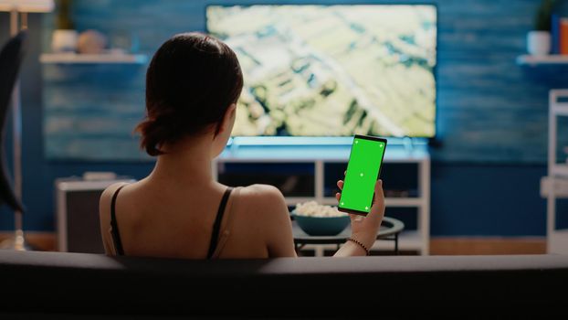 Caucasian woman holding mobile phone with green screen vertically looking at mockup template for chroma key. Young person using modern smartphone with copy space of isolated background