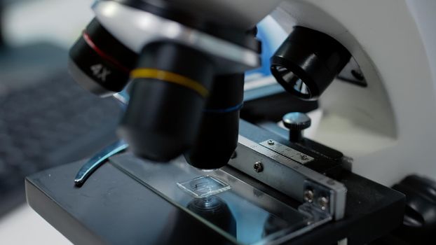 Close up of laboratory microscope with tray for fluid sample research at workplace. Optical instrument with magnifier and glass lenses or tools for genetic dna and blood substance