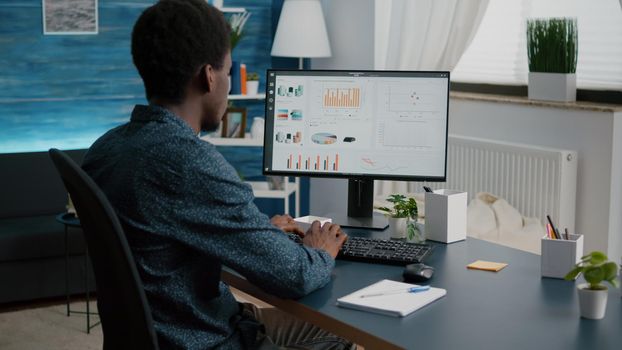 African american man working from home, taking notes on notepad while remote working on PC from living room. Black guy computer user using business internet online web communication job