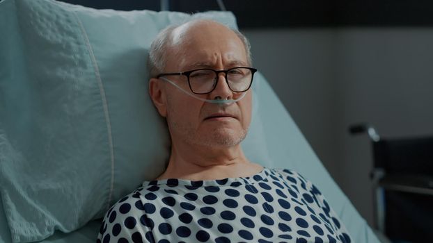 Portrait of ill patient laying in hospital ward at recovery unit with nasal oxygen tube. Old sick man healing from lung disease at medical facility with help from modern equipment