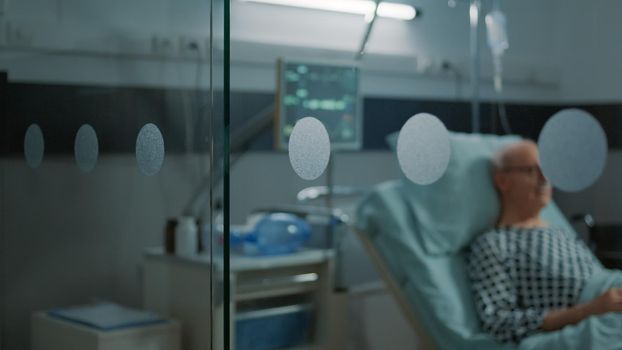 Elderly patient with disease sitting in hospital ward waiting on healthcare system to heal breathing problems. Sick old man sitting in bed with nasal oxygen tube and oximeter to get help