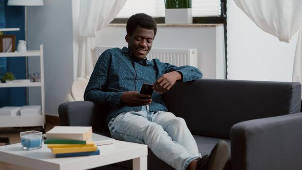 African american man with phone in hands looking at online streaming services content, enjoying working from home, connection via internet web services. Home technology user