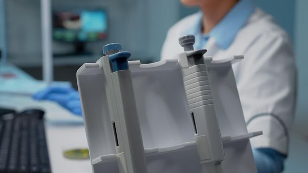 Close up of hand using micropipette in science laboratory for chemical research. Scientist with gloves grabbing dripping instrument for development while sitting at research desk