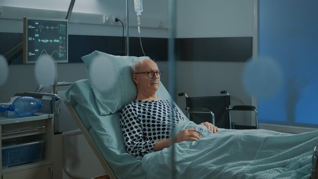 Sick old man staying in hospital ward bed with oximeter and nasal oxygen tube while waiting for medical treatment, medicine. Elderly patient with disease hoping for surgery recovery